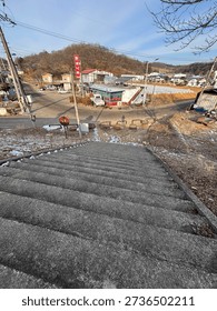 A perspective shot looking down a flight of gray concrete stairs, featuring the long shadow of a person cast by the bright sun onto the ground below.