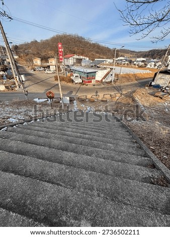 A perspective shot looking down a flight of gray concrete stairs, featuring the long shadow of a person cast by the bright sun onto the ground below.