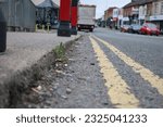 Perspective shot of road surface with pavement, double yellow lines and cars parked in the distance