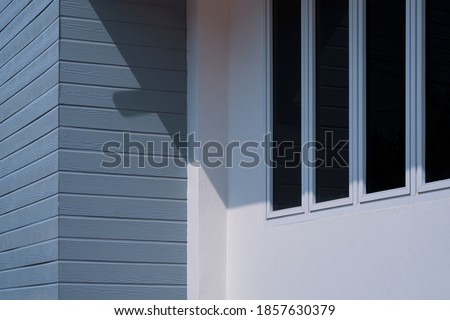 Perspective side view of glass windows on white cement and gray artificial wooden wall outside of house building 