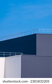 Perspective side view of modern white and gray Corrugated Metal Factory Building with steel fence on rooftop against blue clear sky in vertical frame