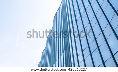 Perspective and underside angle view to textured background of contemporary glass facade of achitecture building skyscrapers with light reflect of sky and cloud. (Detail curve shape of glass mullion)