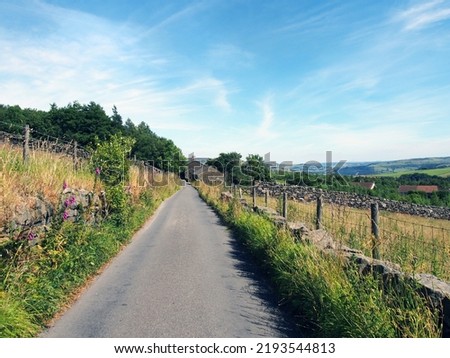 perspective view along a narrow country lane with a stone wall and farmhouse surrounded by fields in summer near the village of colden in calderdale west yorkshire