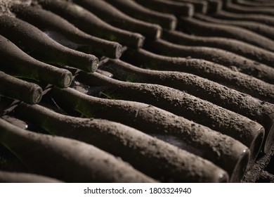 perspective view closeup of stacked aged wine bottles ancient collection covered with soft black mold and spiderweb in vintage wine cellar