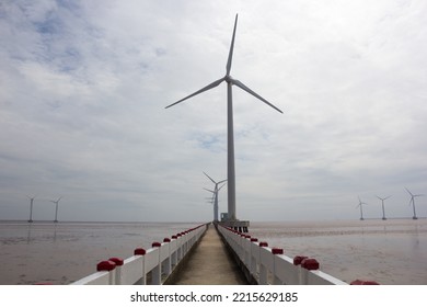 Perspective View Of A Concrete Bridge To Wind Turbines Standing In The Sea On Summer Sunny Day