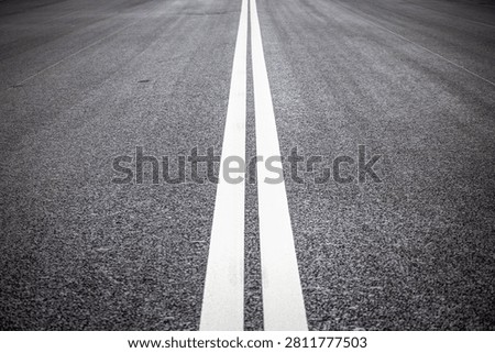 Perspective view of double white solid lines on new asphalt road surface. Symmetric road markings for traffic separation and safety on empty urban highway.
