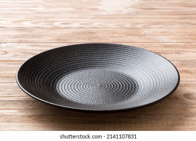 Perspective view of empty black plate on wooden background. Empty space for your design. - Shutterstock ID 2141107831