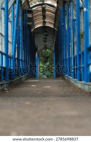 Perspective view of empty blue pedestrian bridge tunnel with steel structure leading to green trees. Urban architecture and leading lines for travel and walkway concept.