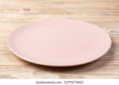 Perspective view. Empty pink matte plate on orange wooden background.