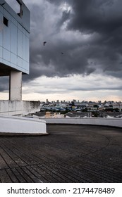 Perspective View Of An Empty Rooftop Car Park Of An Abandoned Mall, Dark Rain Clouds Cover A City In The Backgrounds.