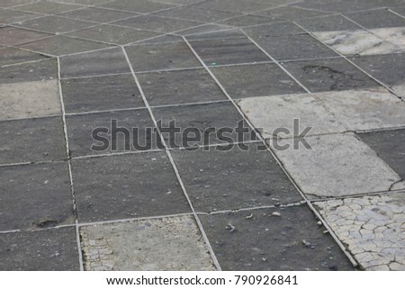 Perspective view of a grey pavment composed of geometric shapes and lines.  Squares and various polygons make a textured surface with reliefs. The soil is ancient and is used by the walkers. 