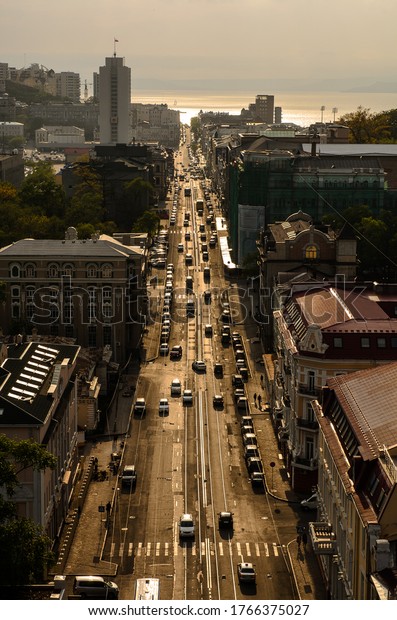 Perspective view of a long central city street\
with with silhouettes of cars and pedestrians people at sunset\
bright sun. Top view\
vertical.