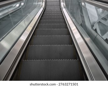 A perspective view looking down a long silver escalator