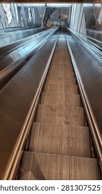 Perspective view looking down a long empty modern steel escalator stairs in a public subway station or mall.