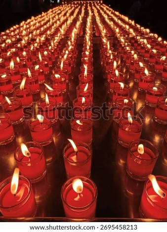 Perspective view of many burning red prayer candles in glass cups, arranged in long symmetrical rows for a spiritual ceremony or vigil.