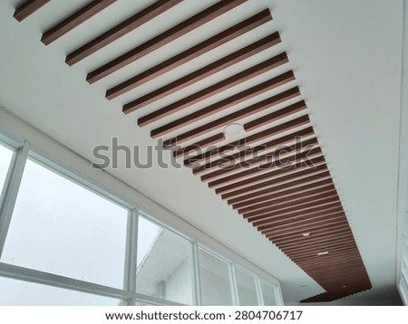 Perspective view of a modern building ceiling decorated with parallel brown wooden slats or baffles, interior design concept featuring large glass windows, white plaster, and minimal aesthetic.