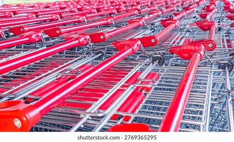 A perspective view of multiple red shopping carts nested together in a long row. The image highlights the metal wire mesh and bright plastic handles.