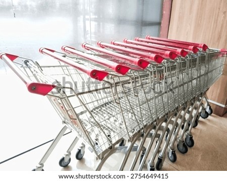 A perspective view of multiple silver shopping trolleys with red handles lined up neatly. Representing consumerism, retail industry, and shopping experience