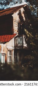 A Perspective View Of An Old Wooden House Corner In The Shadow Of A Rowan Tree. Vertical View Of A Rustic Cabin Backyard On A Sunny Day. A Wooden Cottage With A Selective Focus On Its Old Balcony