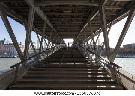 Perspective view on the Léopold-sédar-senghor bridge and its structure in Paris, with a man walking on the bridge.