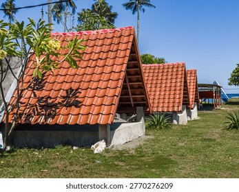 A perspective view of red-roofed triangular buildings leading towards the sea, blending modern design with tropical surroundings and a glimpse of the ocean in the distance.