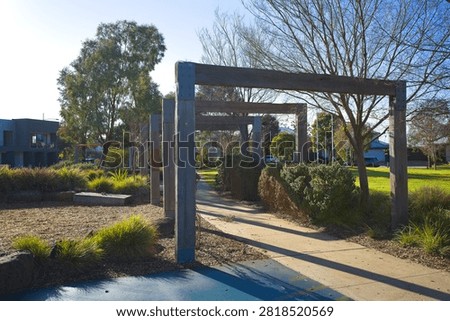 Perspective view of a rustic timber pergola path surrounded by native plants and play areas at Bullion Park in Woodlea Estate, Aintree, Victoria.