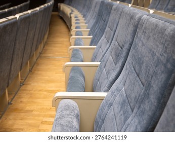 Perspective view showcasing rows empty blue velvet upholstered theater chairs beige armrests curved arrangement polished wooden parquet floor auditorium interior assembly hall.