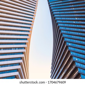 Perspective view of the sky between the twin glass buildings. Sunshine reflection on the glass walls against the blue sky. Close up of black and white similar, modern twisted skyscrapers.