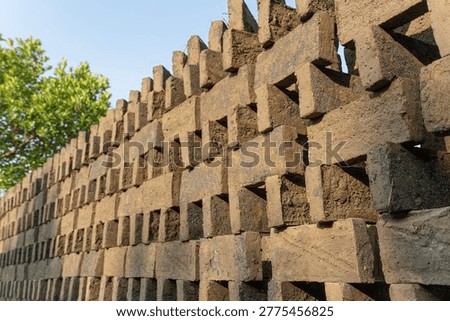 Perspective view of stacked raw clay bricks for drying under a clear blue sky. Traditional rural industry and construction material production.