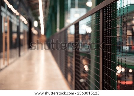 Perspective view of unfocused elevated walkway in loft office building. Mesh fence on the left, glass lass office wall partitions on the right.