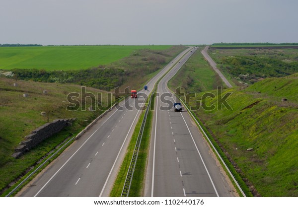 A perspective view of the\
wide empty highway. Cars driving on the road far away. Natural\
colours