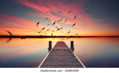 Perspective view of a wooden pier on the pond at sunset with perfectly specular reflection