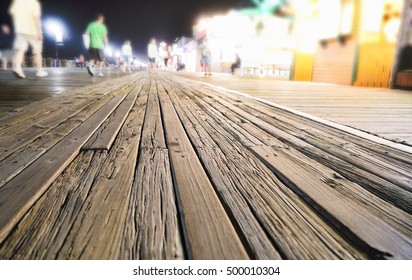 Perspective Of Wooden Boardwalk At Night With Food Vendors And Rides In The Background