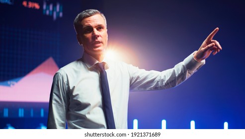 Persuasive mature man gesticulating and talking about financial charts from stage during business seminar