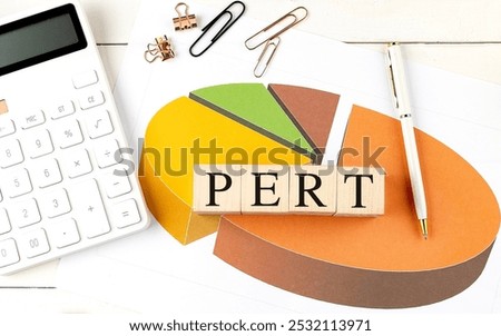 PERT program evaluation review technique wooden blocks on a pie chart with a calculator, pen, and paper clips on desk . 