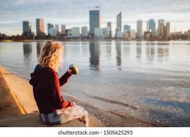 Perth, Australia - September 14th, 2019 : Early Morning Sunrise As Fit Girl Finishes Her Run By Drinking A Coffee From A Reusable Cup. The Sun Is Rising Over The Swan River With The City Behind. 