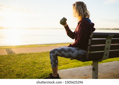 Perth, Australia - September 14th, 2019 : Early Morning Sunrise As Fit Girl Finishes Her Run By Drinking A Coffee From A Reusable Cup. The Sun Is Rising Over The Swan River With The City Behind. 