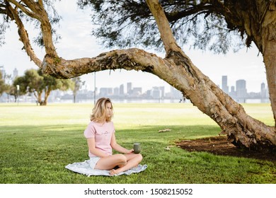 Perth, Western Australia - 14th September, 2019 : Beautiful Girl Drinking Coffee From A Reusable Eco Friendly Cup On The South Perth Foreshore. Early Morning In A Park With The City In The Background.