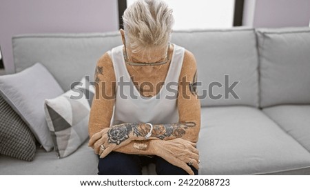 Perturbed mature grey-haired woman chilling solo on her cozy sofa at home, engrossed in deep thought