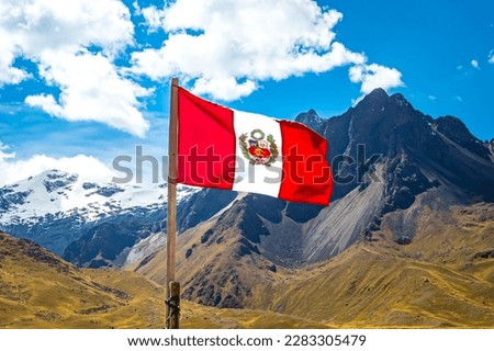 The Peruvian flag flutters in the wind in front of the majestic La Raya mountain range with the snow-capped peak of Chimboya in the background, a proud symbol of the nation's freedom and independence.