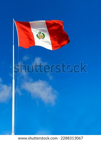 Peruvian flag on the pole fluttering in the wind under a blue sky.