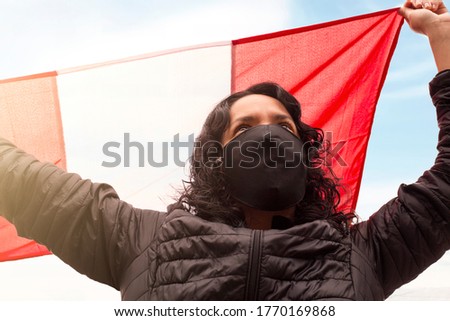 Peruvian woman with mask holds the Peruvian flag with her hands up
