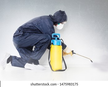 a pest control contractor or exterminator with a chemical tank and spray equipment on the knees spray his chemicals against pests, bugs and mold on the ground in his typical safety dress for work