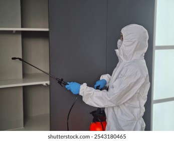 Pest control technician sanitizing a shelf in a modern home using a spray device during daytime - Powered by Shutterstock