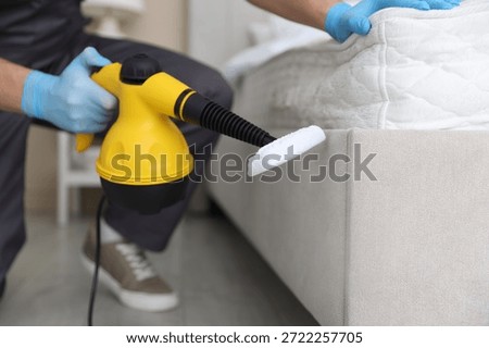 Pest control worker cleaning bed with steam cleaner indoors, closeup