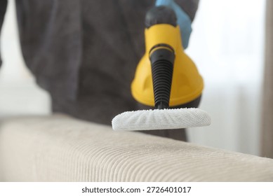 Pest control worker cleaning sofa with steam cleaner indoors, closeup