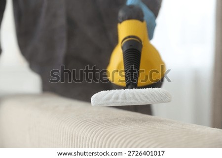 Pest control worker cleaning sofa with steam cleaner indoors, closeup
