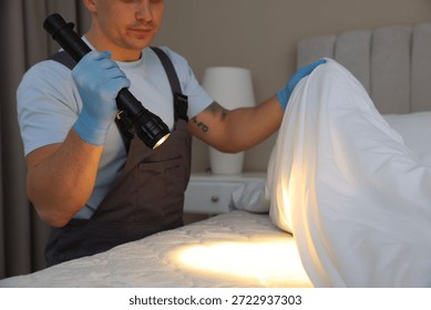 Pest control worker examining bed with flashlight indoors, closeup