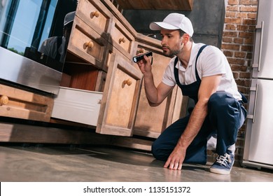 Pest Control Worker Examining Kitchen With Flashlight