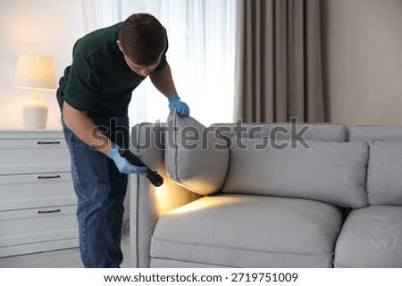 Pest control worker examining sofa with flashlight indoors